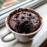 Close-up of a moist chocolate mug cake topped with melted chocolate chips, ready to eat.