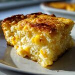 Close-up of a moist slice of cornbread casserole featuring visible whole corn kernels and a golden, slightly caramelized top.