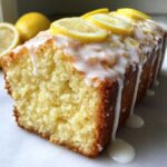 Close-up of a freshly baked lemon pound cake drizzled with white glaze and topped with lemon slices.