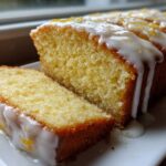 Close-up of a sliced lemon pound cake drizzled with white lemon glaze and zest.