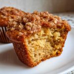 Close-up of a moist oatmeal muffin cut in half, showing the tender interior and a thick, sugary crumb topping.