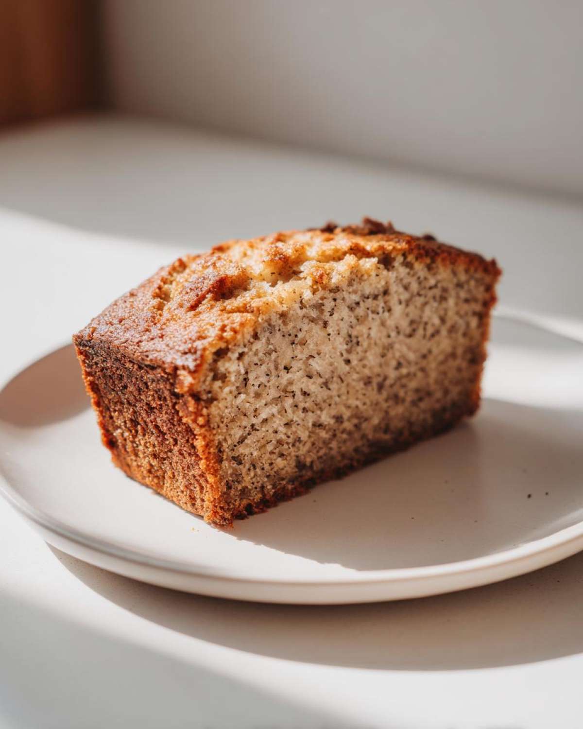 A single, moist slice of sugar free banana bread with a golden crust, sitting on a light-colored plate.