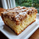 Close-up of a moist slice of sour cream coffee cake topped with cinnamon streusel and a white glaze.