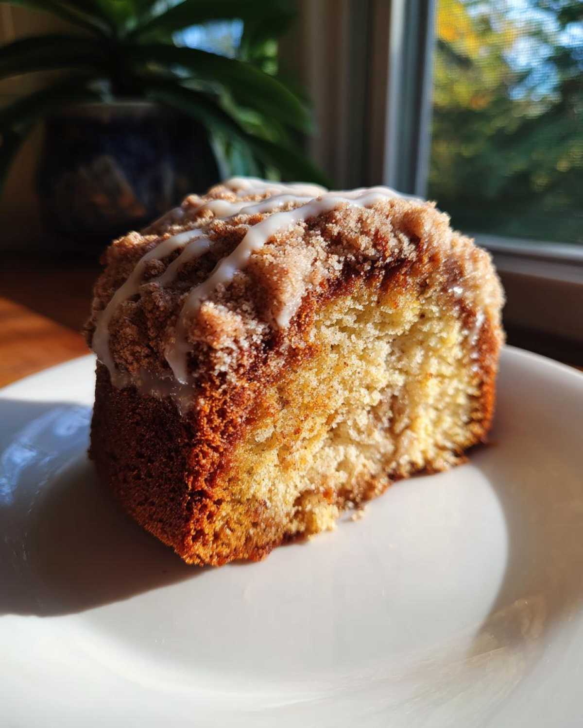A close-up of a moist slice of sour cream coffee cake topped with cinnamon streusel and vanilla glaze.