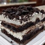 Close-up of a layered slice of amazing oreo dirt cake showing dark chocolate cake, white cream, and crushed cookie topping.