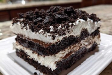 Close-up of a layered slice of amazing oreo dirt cake showing dark chocolate cake, white cream, and crushed cookie topping.