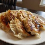 A plate of golden-brown, pan-fried Traditional Chinese Dumplings with crispy bottoms.