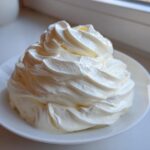 A dollop of thick, rich cream, representing a key ingredient for homemade alfredo sauce, piped onto a small white plate.