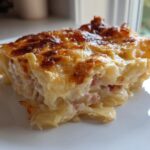 A close-up of a baked slice of creamy scalloped potatoes and ham with a golden-brown cheesy top.