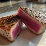 Two halves of a seared tuna steak showing a vibrant pink, rare center, coated in a flavorful herb and spice MARINADE FOR TUNA STEAK crust.