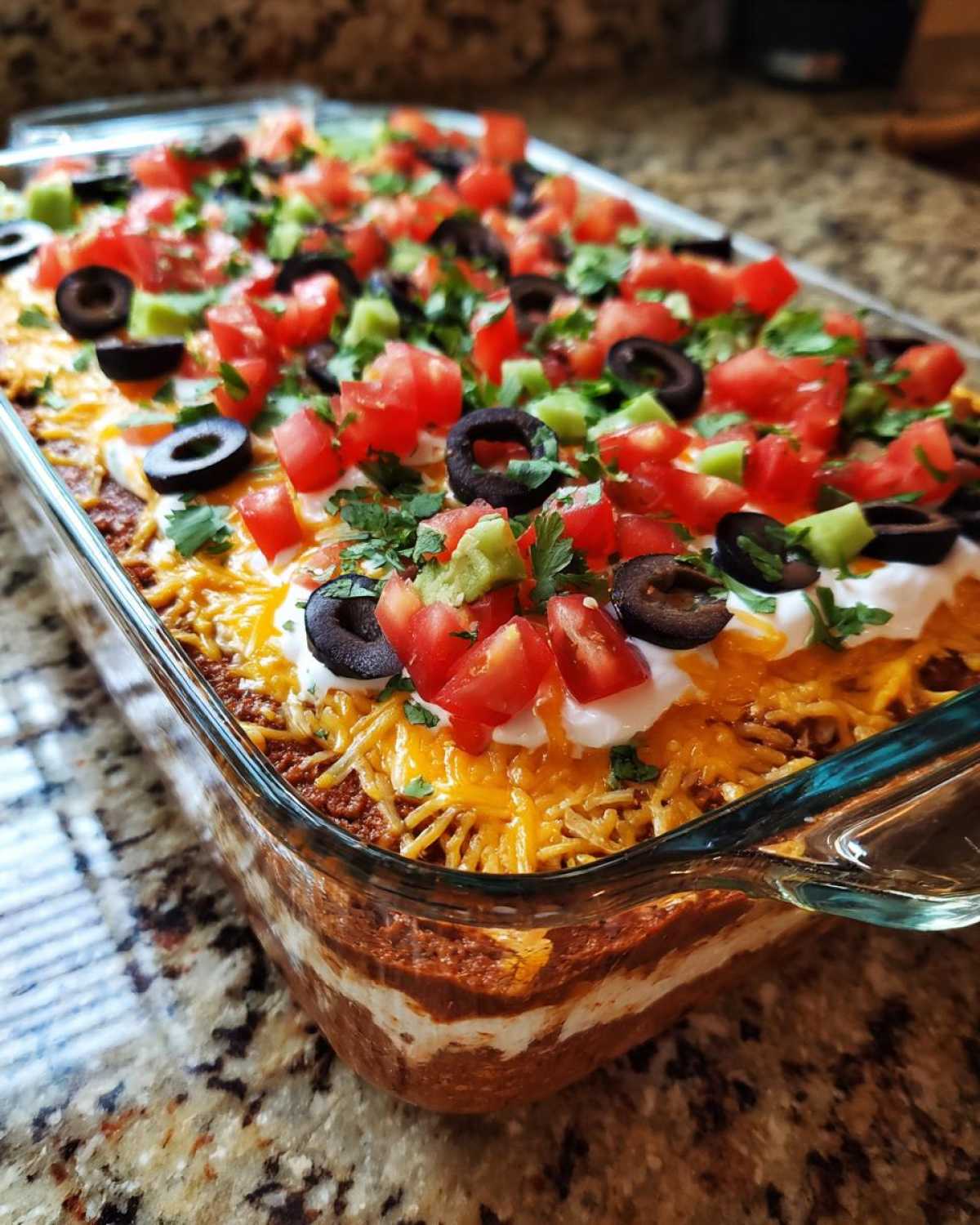 Close-up of a fully assembled Seven layer dip in a clear glass dish, topped with tomatoes, olives, and sour cream.