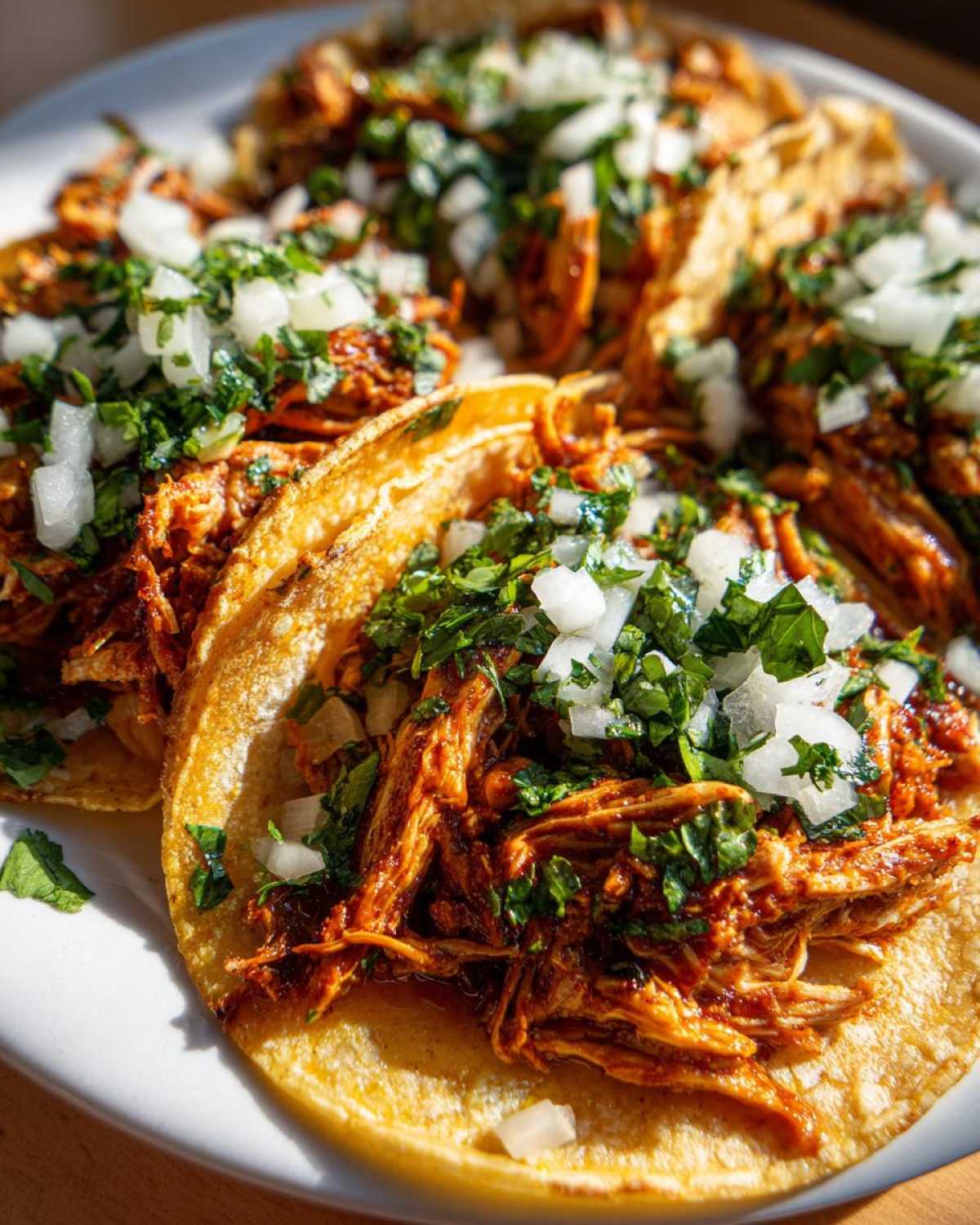 Close-up of several flavorful chicken tacos filled with shredded orange chicken, topped with fresh diced white onion and cilantro.