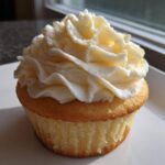 A single, moist vanilla cupcake topped with a generous swirl of creamy white vanilla frosting.
