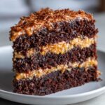 Close-up of a decadent slice of german chocolate cake recipe showing three layers of dark chocolate cake and coconut-pecan frosting.