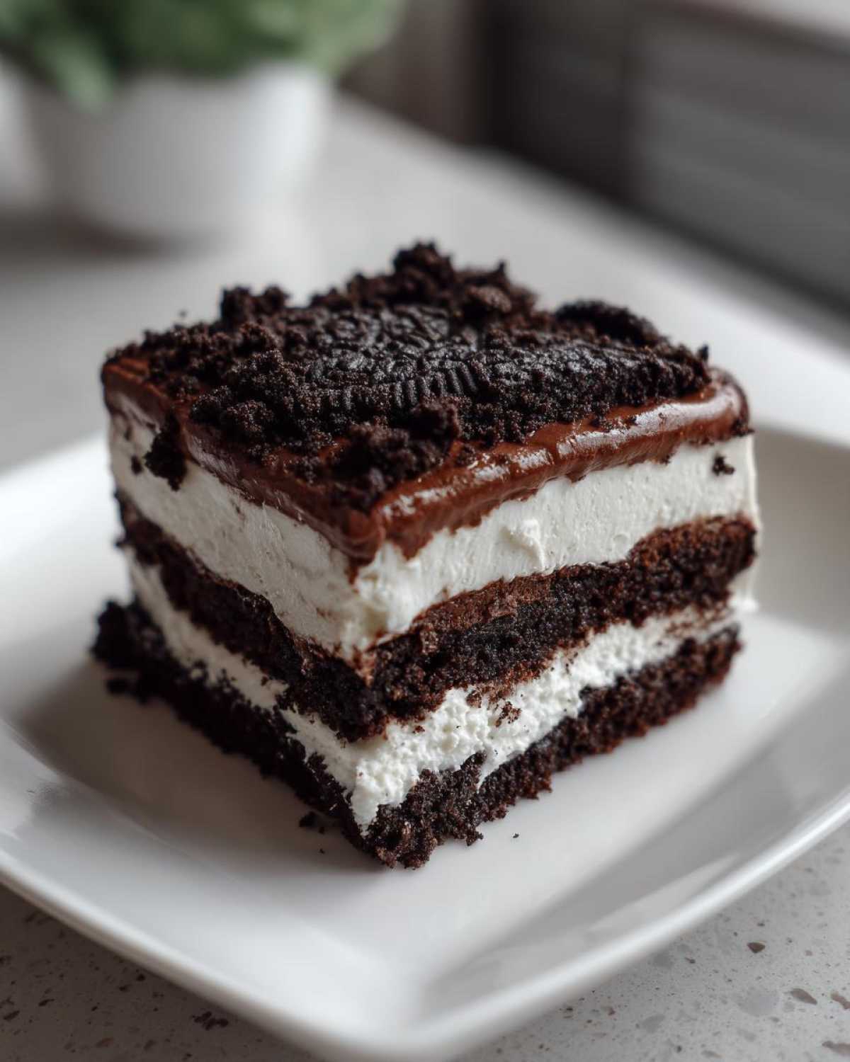 A square slice of layered oreo dirt cake showing chocolate cake, white cream filling, and crushed cookie topping.