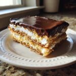 A layered slice of eclair cake with graham cracker crust, cream filling, and chocolate glaze.