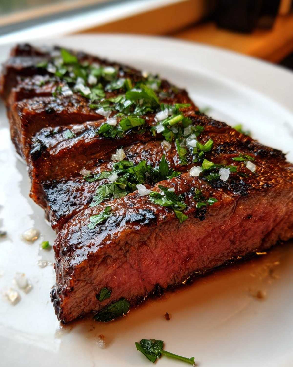Close-up of sliced, medium-rare steak showing a juicy interior, topped with fresh cilantro and onion, likely prepared with carne asada marinade.