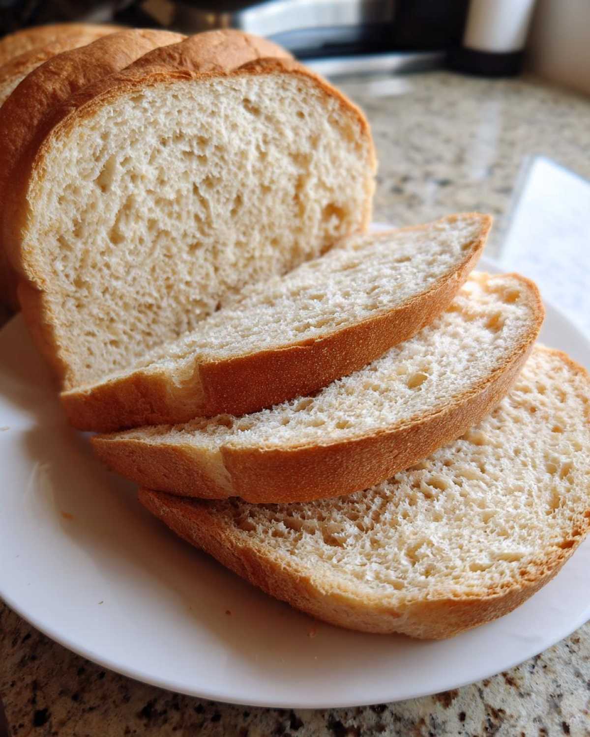 Close-up of a freshly baked loaf of whole wheat bread, partially sliced and arranged on a white plate.