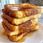 Close-up of a tall stack of golden brown easy french toast slices drizzled generously with maple syrup.
