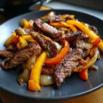 Close-up of perfectly cooked, sliced steak fajitas mixed with sautéed yellow and orange bell peppers and onions.