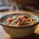 A steaming bowl of thick Ham and Bean Soup topped with shredded ham, carrots, and celery.