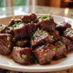 Close-up of tender, cubed crockpot steak bites coated in a rich sauce and sprinkled with fresh parsley.