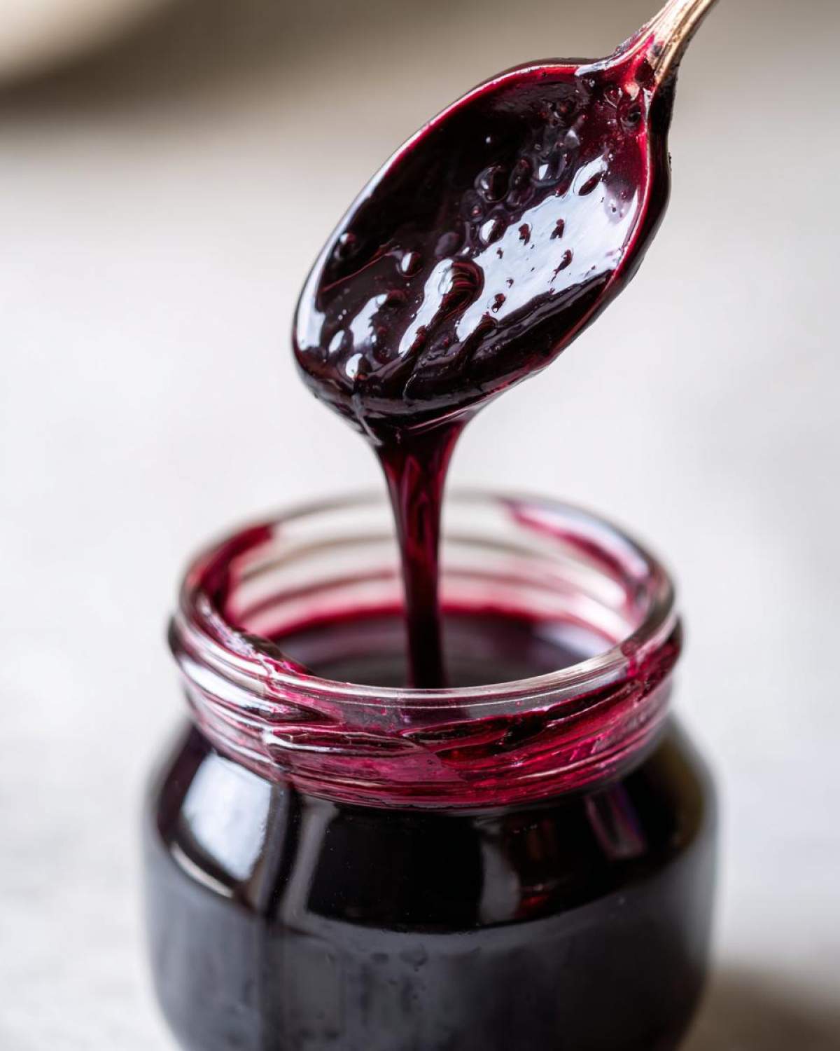 Close-up of thick, dark purple elderberry syrup recipe being spooned back into a glass jar.