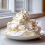 A large, fluffy mound of freshly made vanilla buttercream frosting sitting on a white plate.