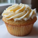 A close-up shot of a single, perfectly baked vanilla cupcake topped with rich, swirled vanilla frosting.