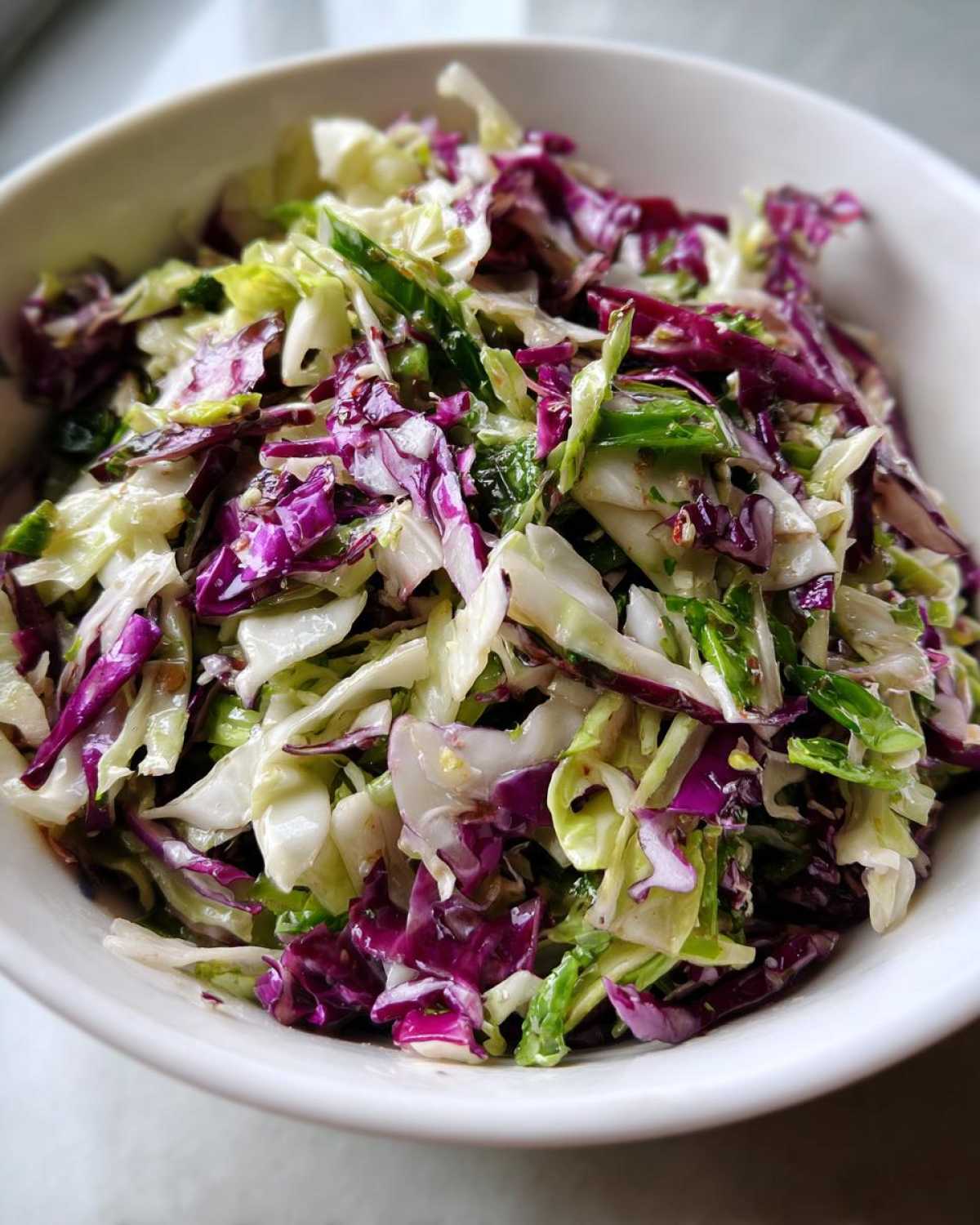 Close-up of a fresh, colorful cabbage salad featuring shredded red and green cabbage in a white bowl.