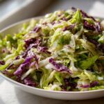 Close-up of a vibrant, freshly dressed cabbage salad featuring shredded green and purple cabbage.