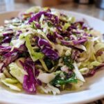 Close-up of a fresh, vibrant cabbage salad featuring shredded green and purple cabbage tossed with herbs and a light dressing.