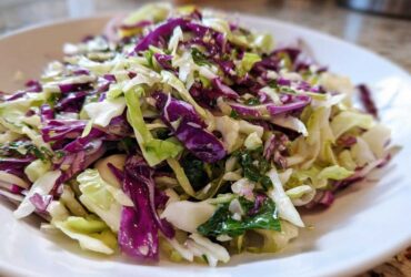 Close-up of a fresh, vibrant cabbage salad featuring shredded green and purple cabbage tossed with herbs and a light dressing.