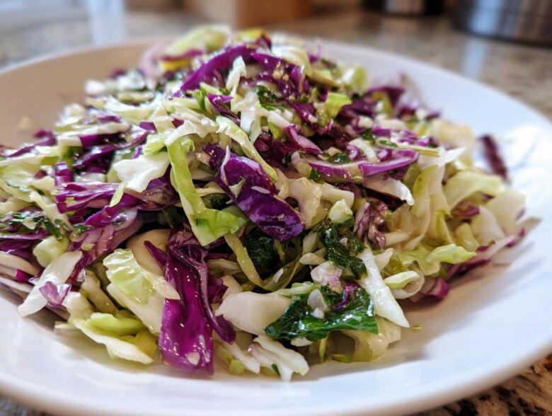 Close-up of a fresh, vibrant cabbage salad featuring shredded green and purple cabbage tossed with herbs and a light dressing.