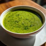 A vibrant, bright green cilantro lime sauce served in a small white bowl on a wooden table.