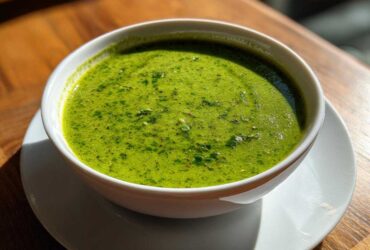 A vibrant, bright green cilantro lime sauce served in a small white bowl on a wooden table.