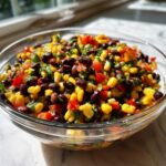 Close-up of a clear glass bowl filled with colorful cowboy caviar, featuring black beans, corn, and diced red peppers.