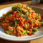 A close-up of a vibrant, textured crispy rice salad mixed with shredded carrots, edamame, and fresh mint leaves.
