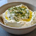 Close-up of creamy whipped feta dip in a bowl, drizzled with olive oil and topped with fresh dill.