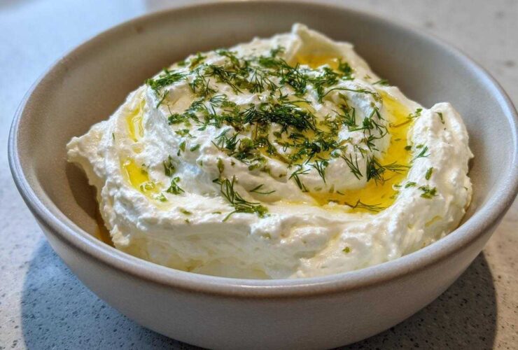 Close-up of creamy whipped feta dip in a bowl, drizzled with olive oil and topped with fresh dill.