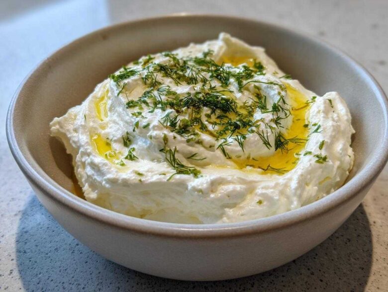 Close-up of creamy whipped feta dip in a bowl, drizzled with olive oil and topped with fresh dill.