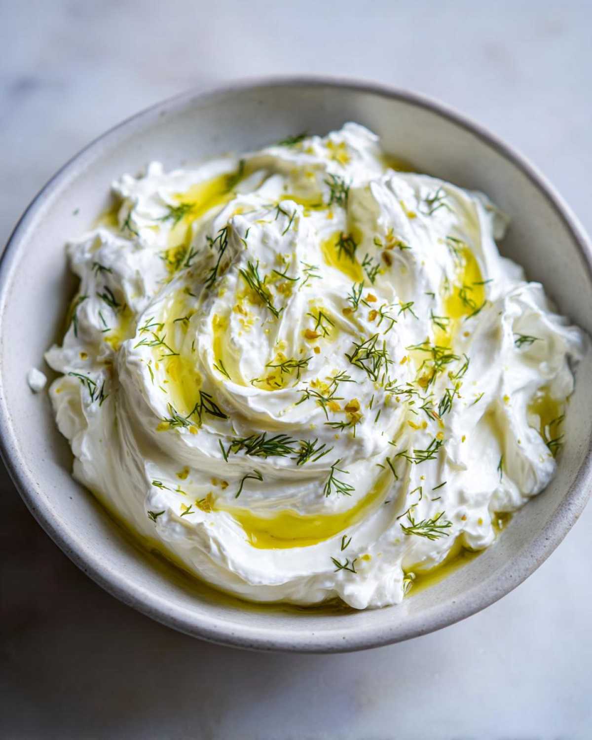 Close-up of creamy whipped feta dip swirled in a bowl, drizzled with olive oil and topped with fresh dill.