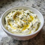 Close-up of a bowl of creamy whipped feta dip drizzled with olive oil and sprinkled with fresh dill.