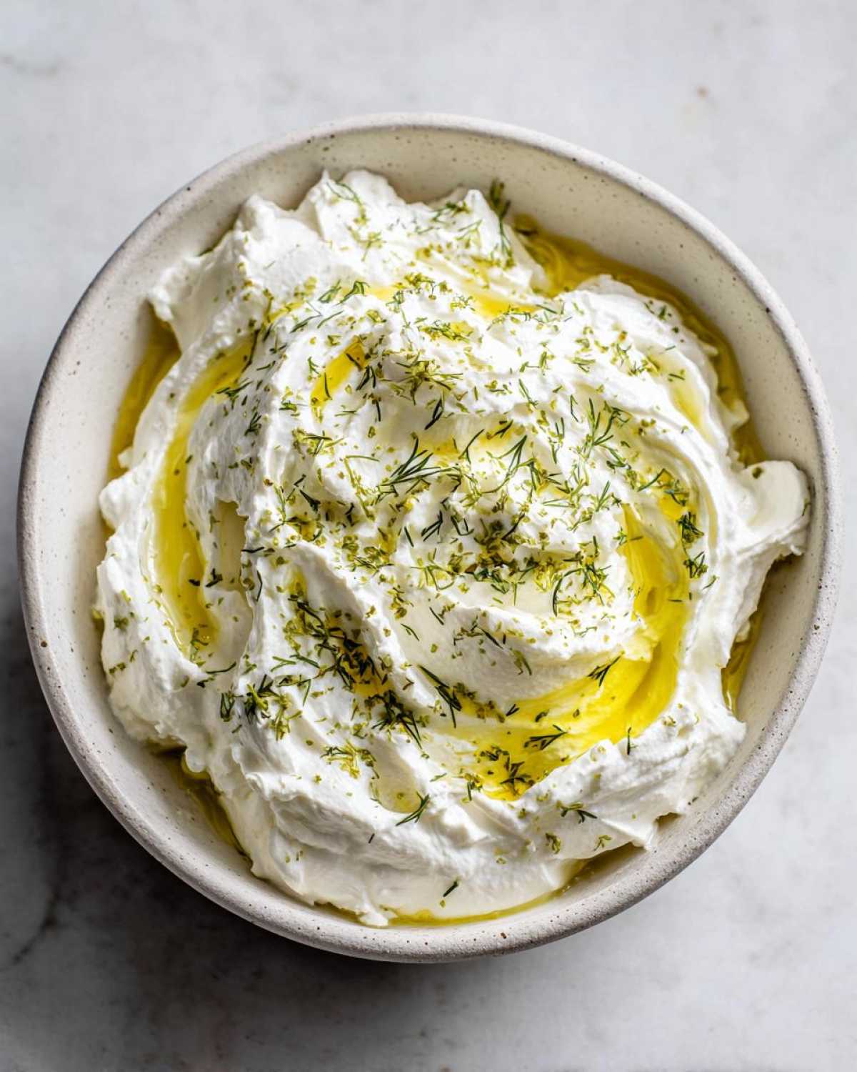 Overhead view of a bowl filled with creamy whipped feta dip, drizzled with olive oil and sprinkled with dill.