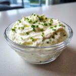 A close-up of thick, creamy 5-Minute Greek Yogurt Ranch Dip topped with freshly chopped chives in a clear glass bowl.
