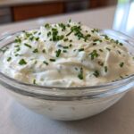 A clear glass bowl filled with creamy 5-Minute Greek Yogurt Ranch Dip, topped generously with fresh chopped chives.