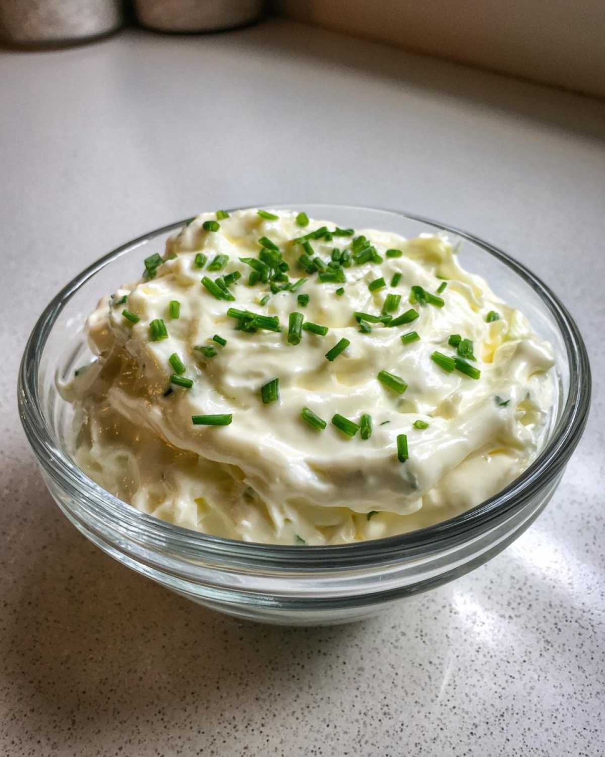 A close-up of creamy 5-Minute Greek Yogurt Ranch Dip topped with fresh, finely chopped green chives in a clear glass bowl.