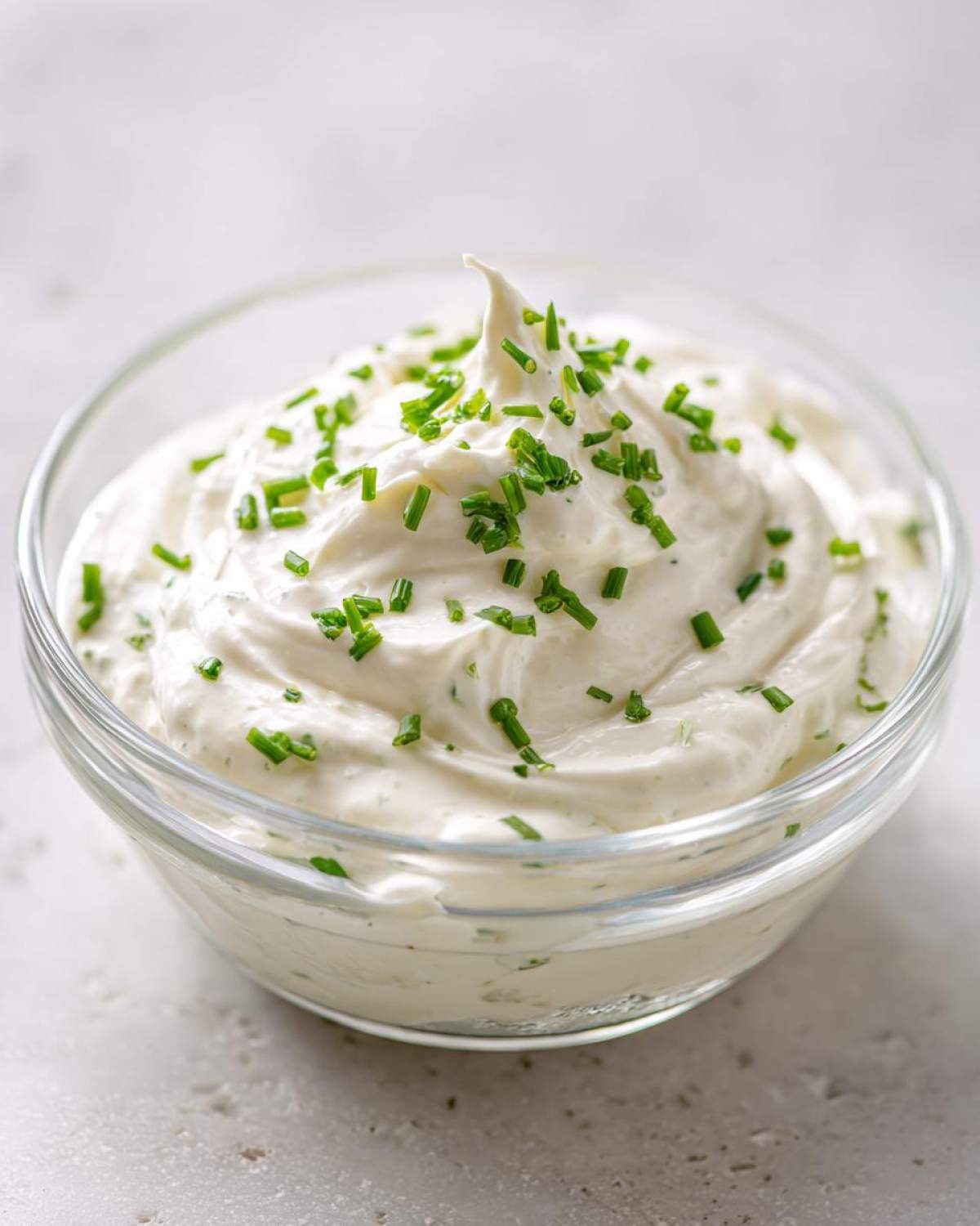 A close-up of thick, creamy 5-Minute Greek Yogurt Ranch Dip topped generously with fresh, chopped chives in a clear glass bowl.