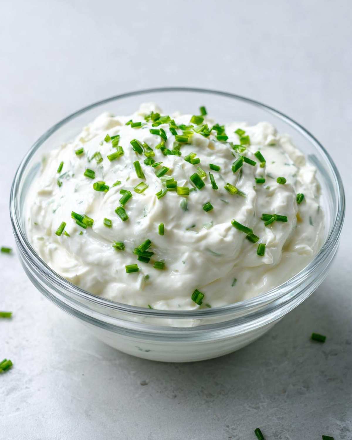 A clear glass bowl filled with thick, creamy 5-Minute Greek Yogurt Ranch Dip, topped with fresh chopped chives.