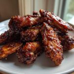A pile of crispy, glazed Air Fryer BBQ Chicken Wings sprinkled with sesame seeds on a white plate.